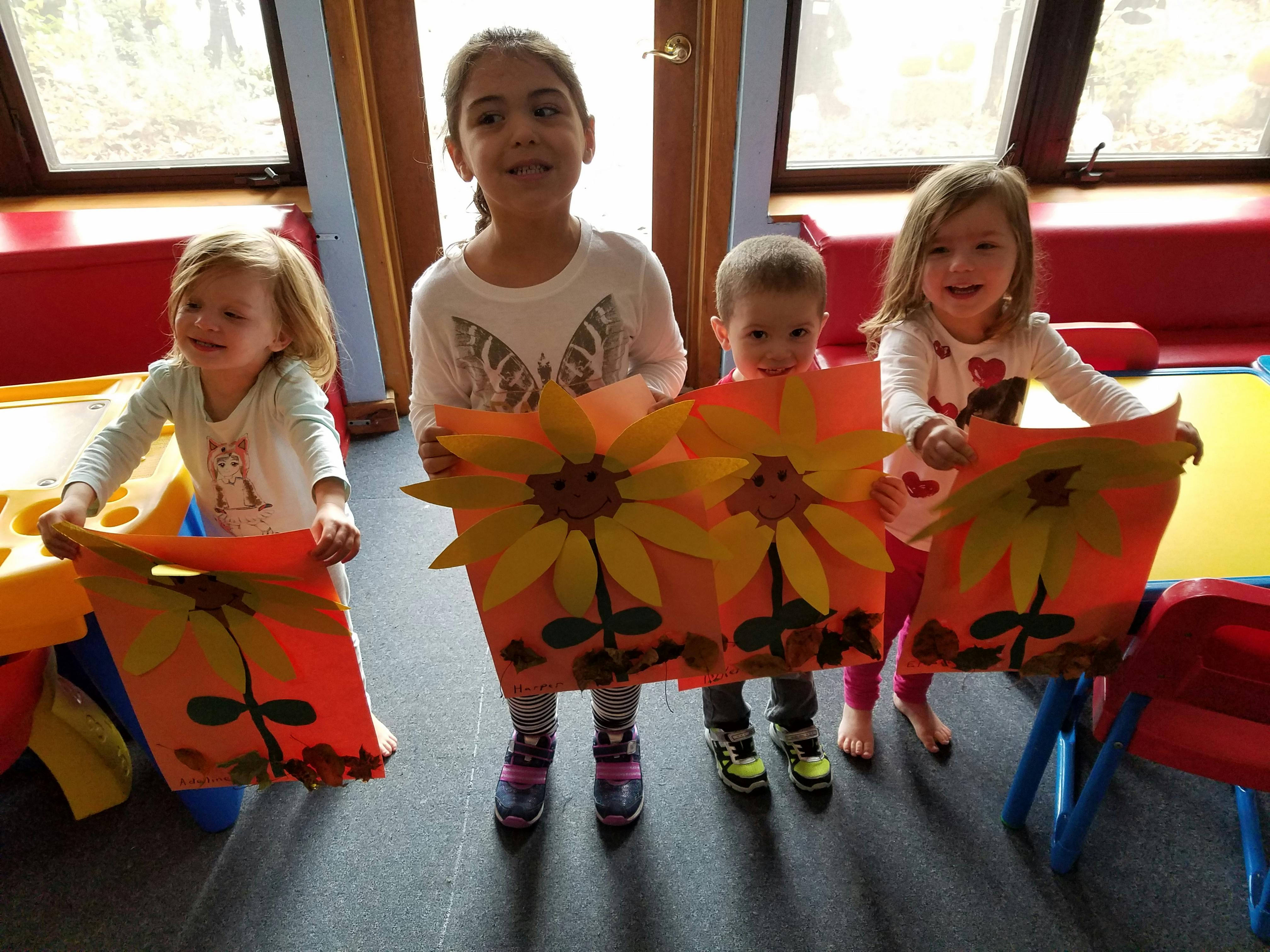Four children holding up paper crafts with sunflowers