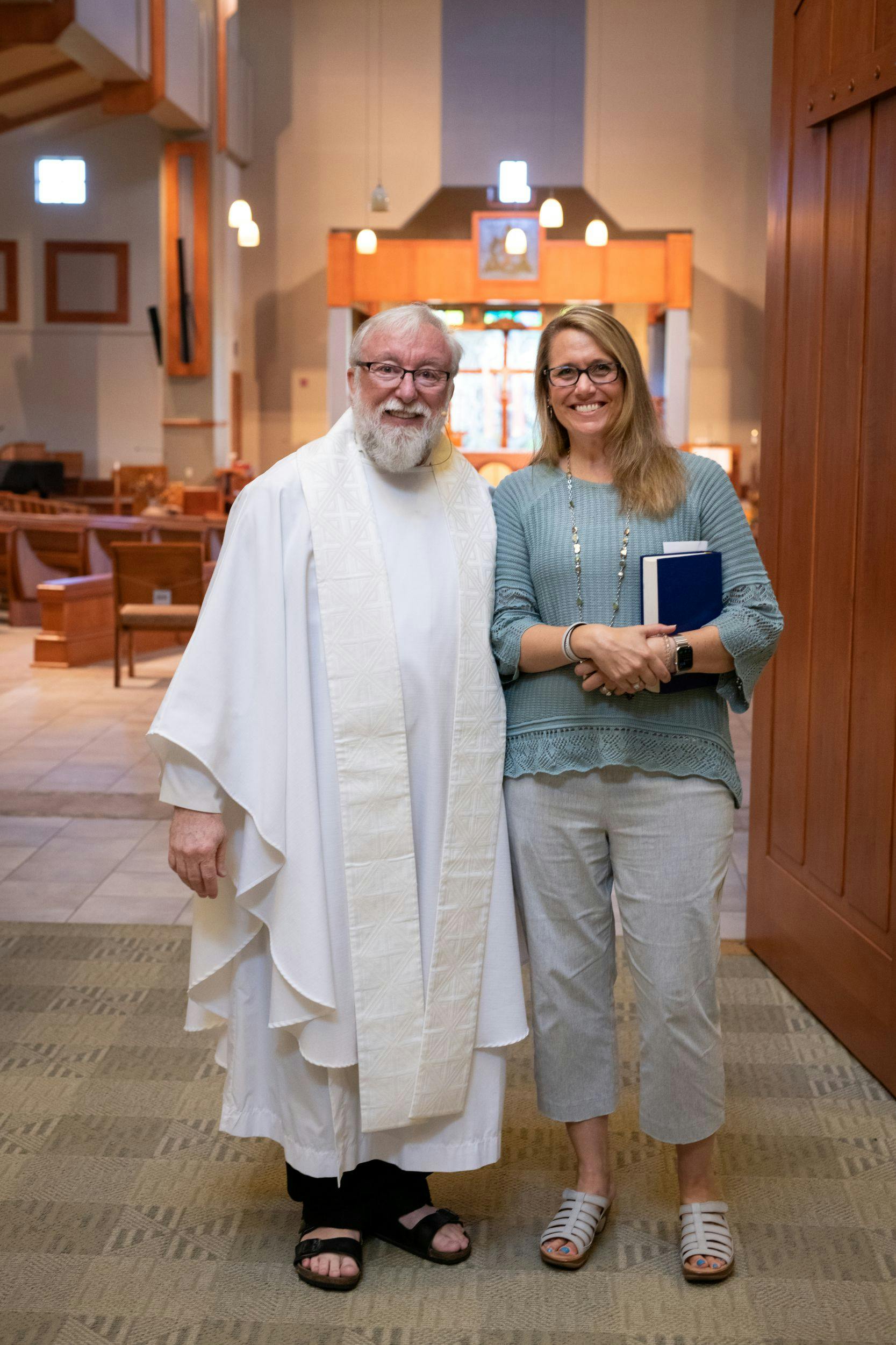 Two people standing in a church, one in a white robe and the other holding a book