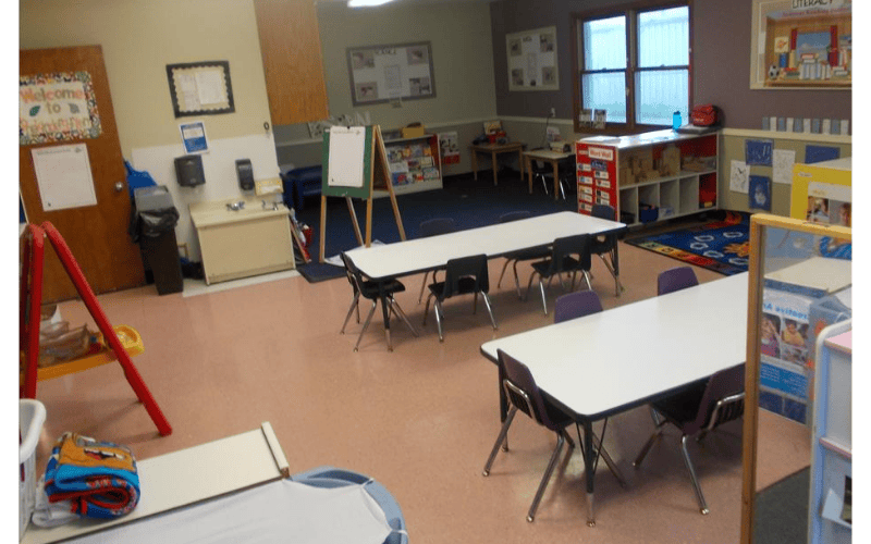 Empty classroom with multiple tables, chairs, and learning materials