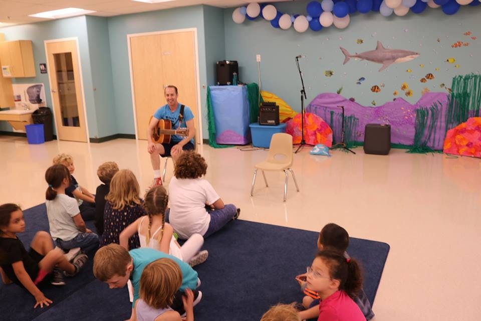Person playing guitar for a group of children in a classroom