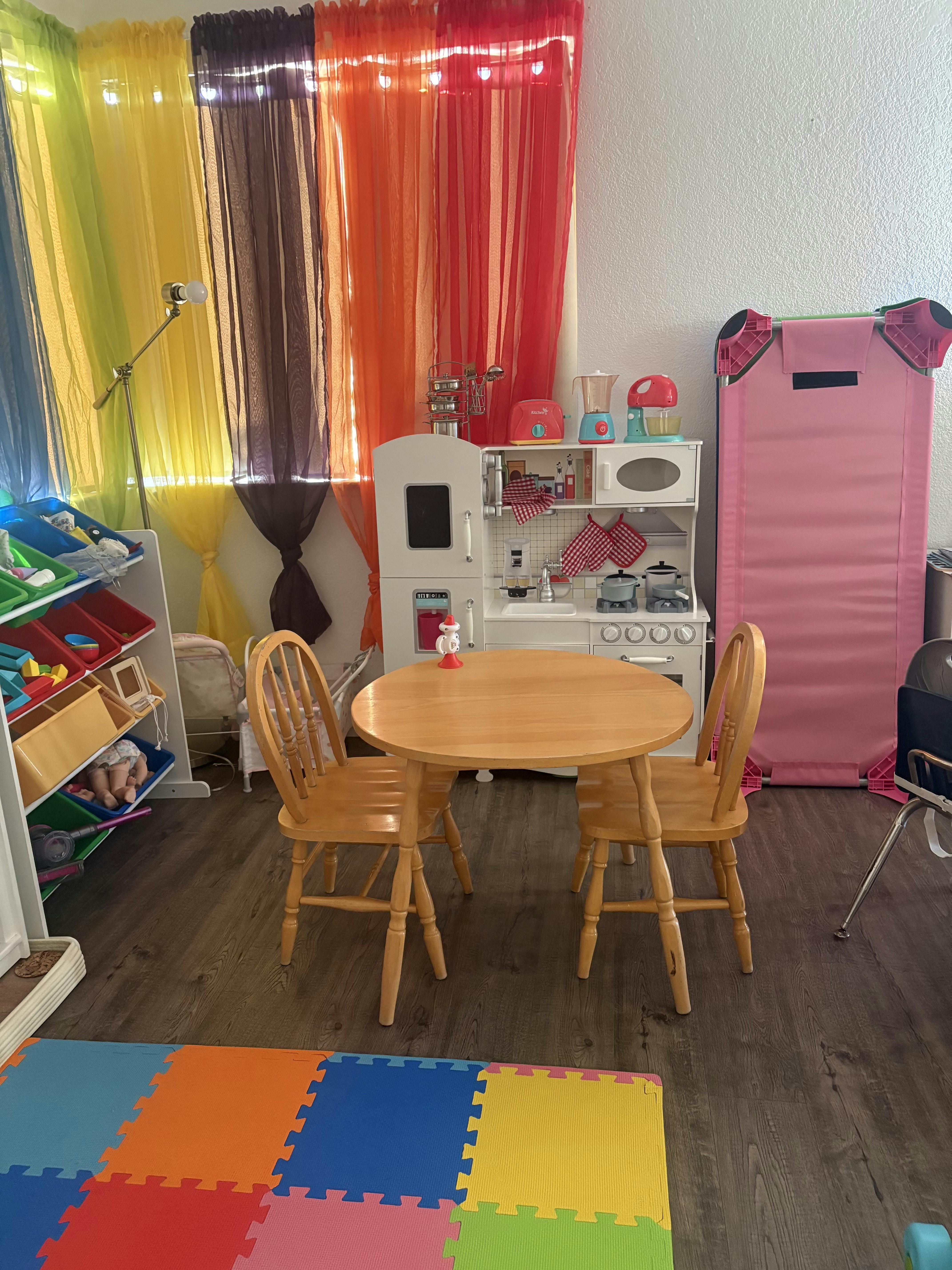 Children's play area with a toy kitchen, round table with two chairs, and colorful curtains