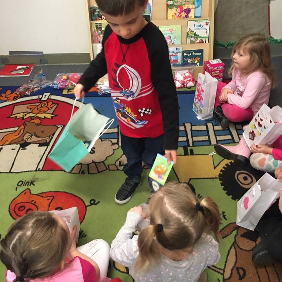 Child holding a gift bag and card, surrounded by other children