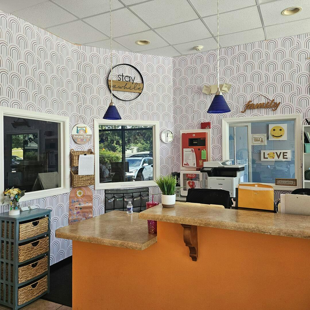 Reception area with an orange counter and rainbow patterned wallpaper, stay awhile sign