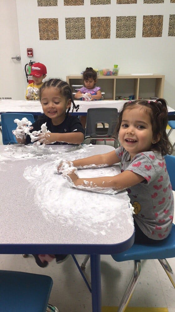 Two children playing with white foam at a table in a classroom