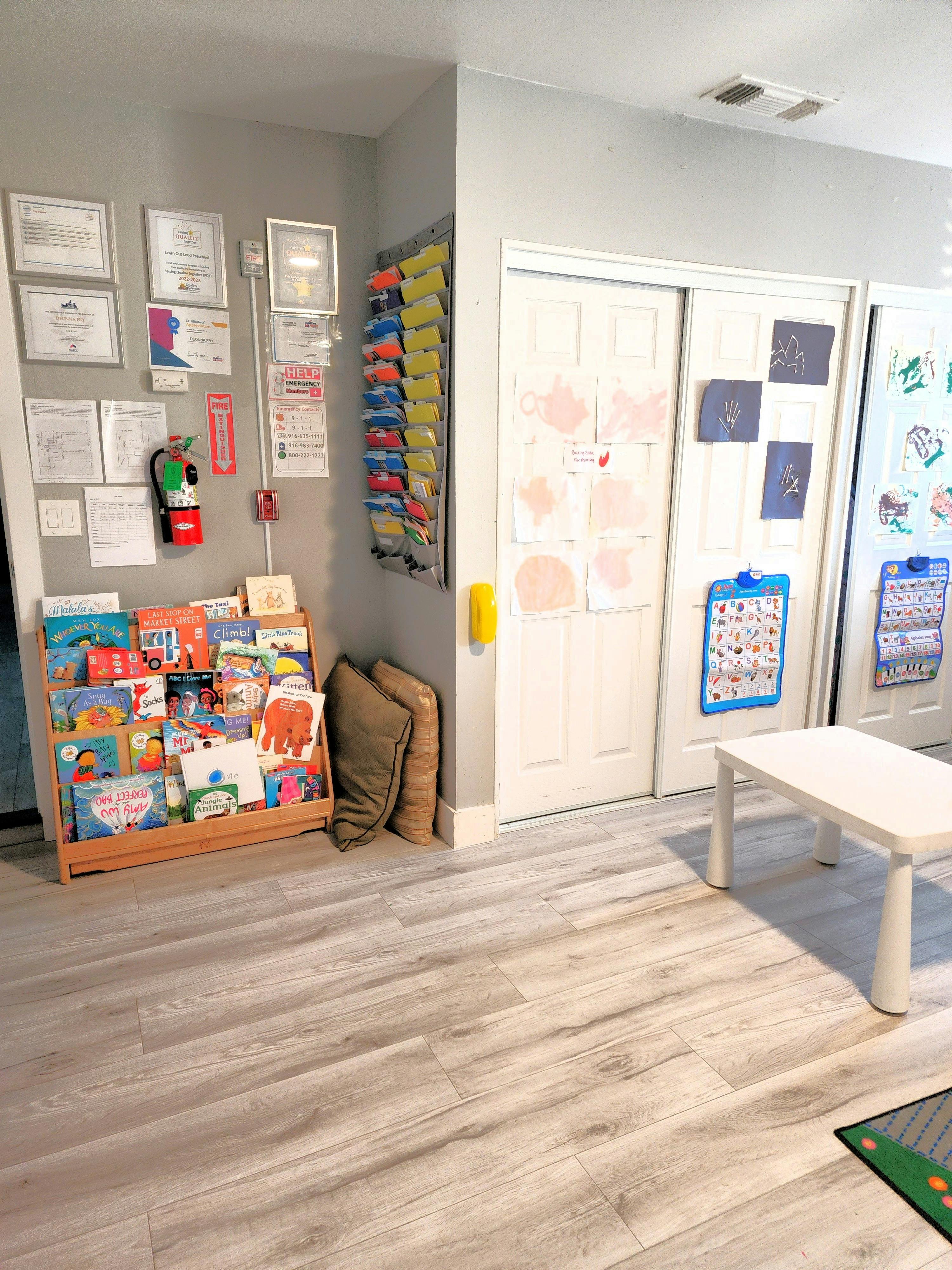 Children's book display, wall with framed documents, and white table in a room