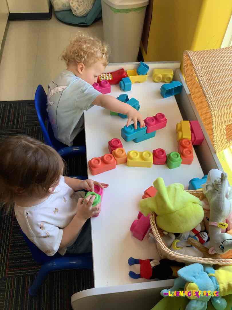 Two children playing with colorful building blocks at a white table