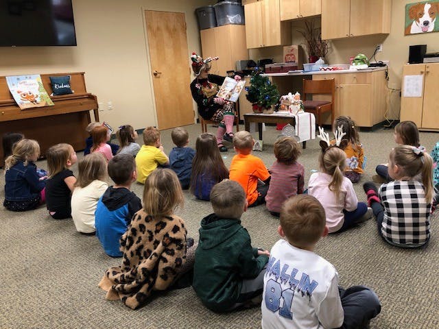Person reading a book to a group of children sitting on the floor