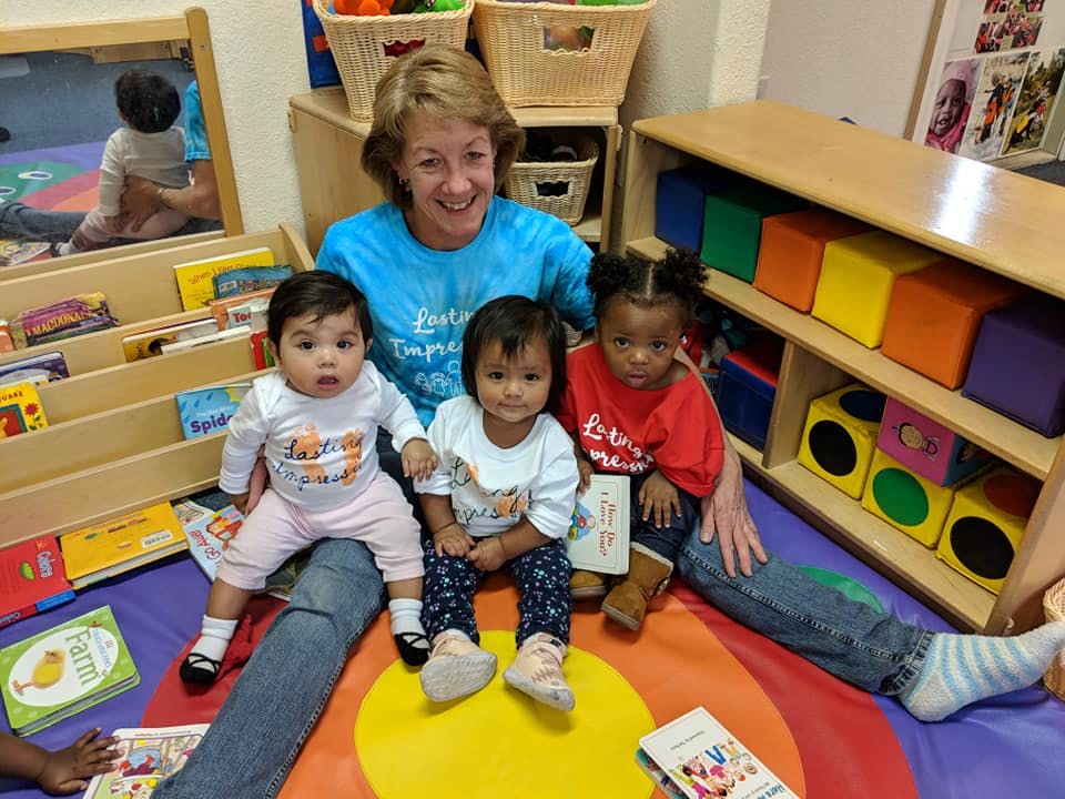 Adult and three young children sitting on a colorful mat in a classroom