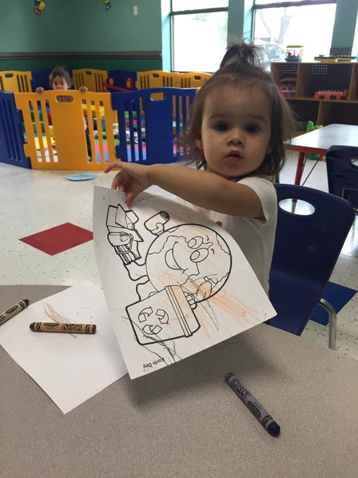 Child holding up a partially colored drawing of a cartoon earth