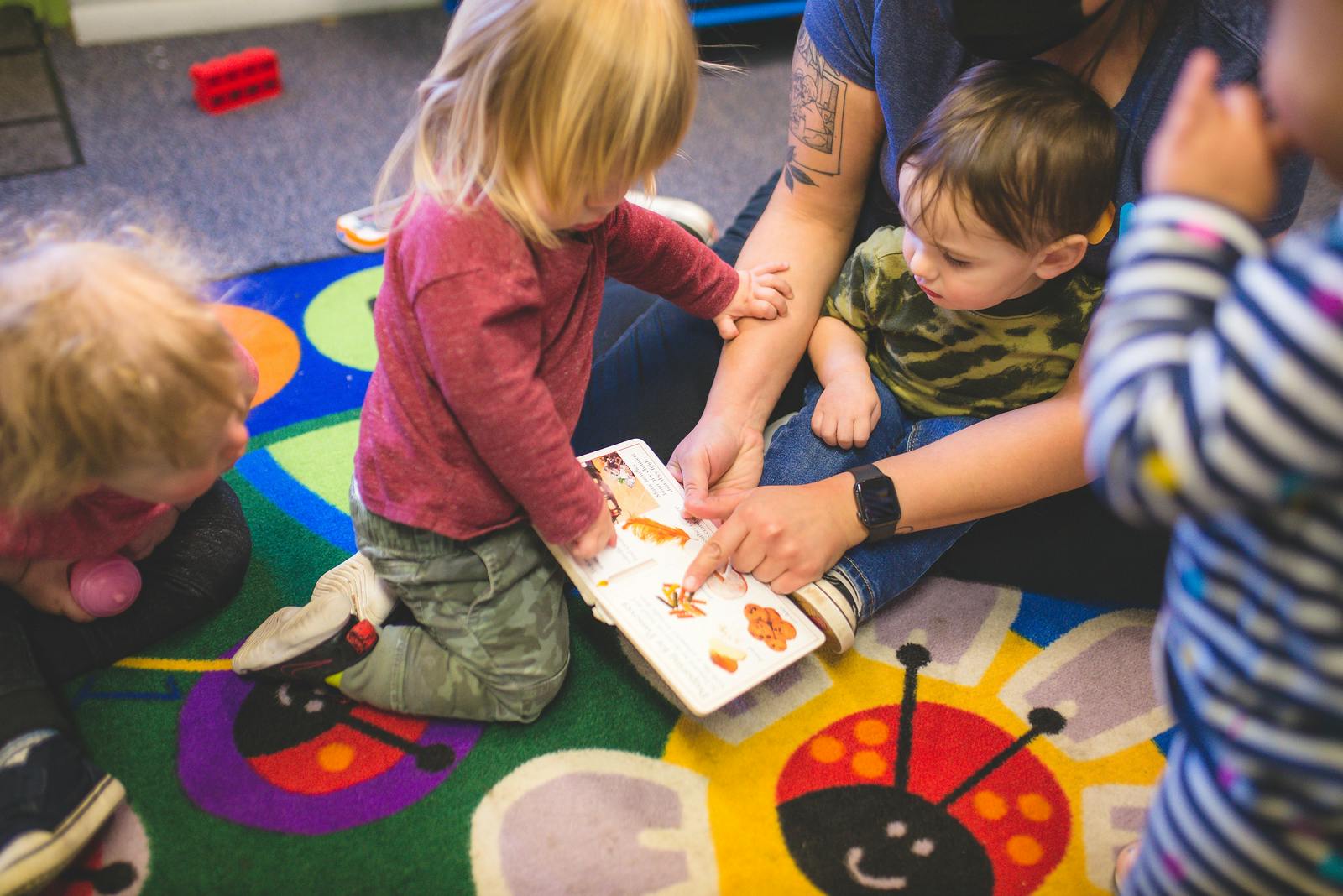 Adult and children looking at a book on a colorful rug