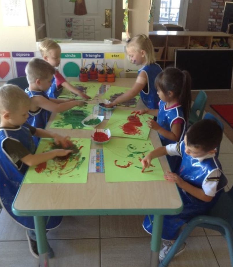 Children finger painting at a table in a classroom