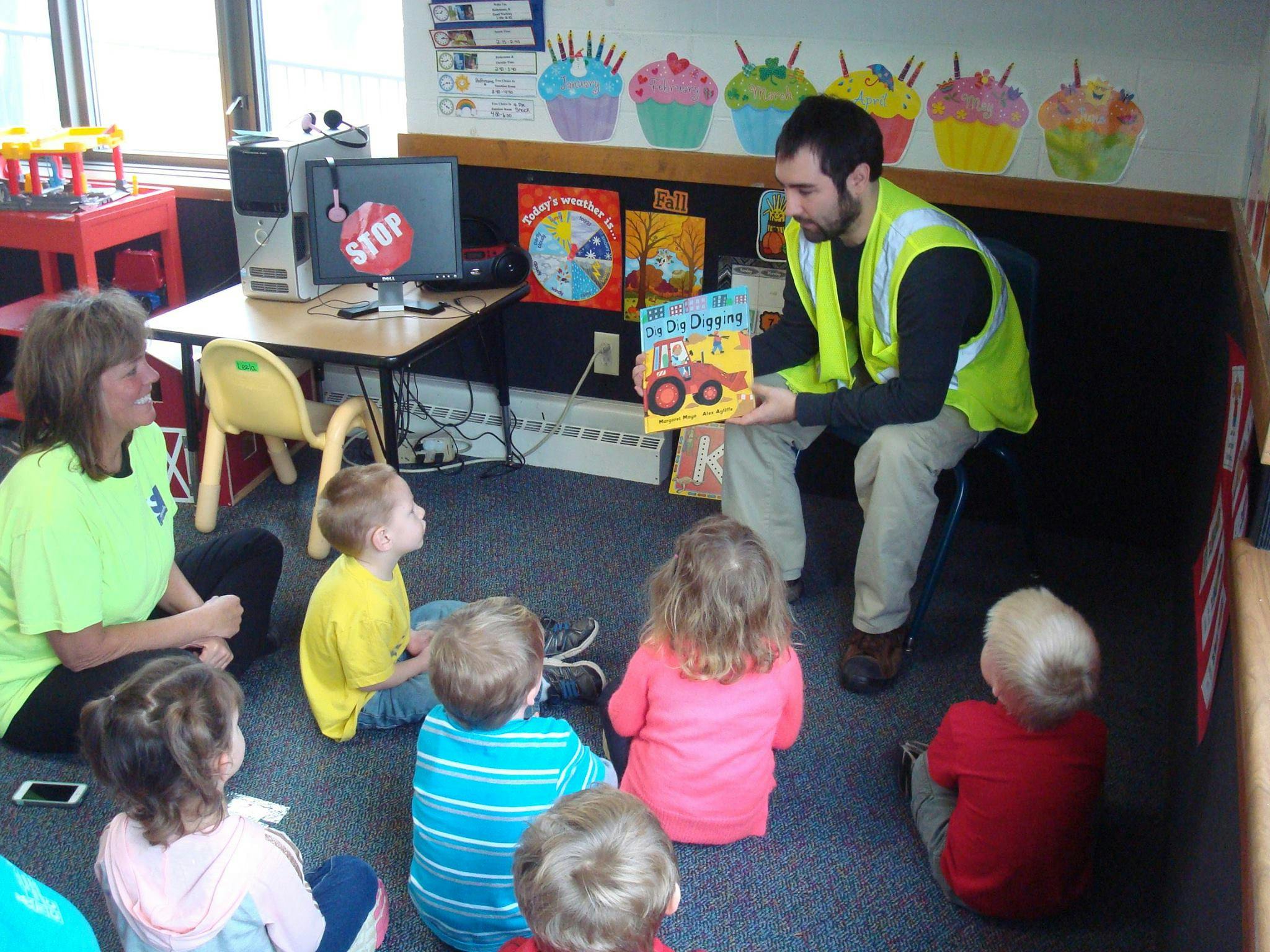 Person in safety vest reading a book to children in a classroom