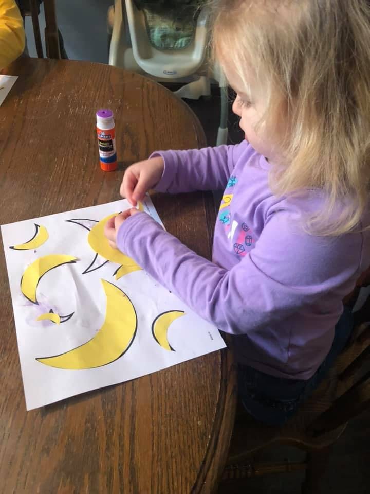 Child gluing yellow crescent shapes onto a white paper