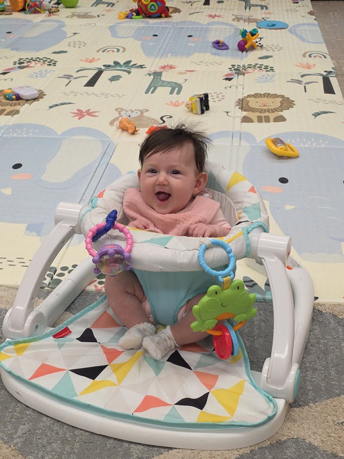 Child sitting in a floor seat surrounded by toys
