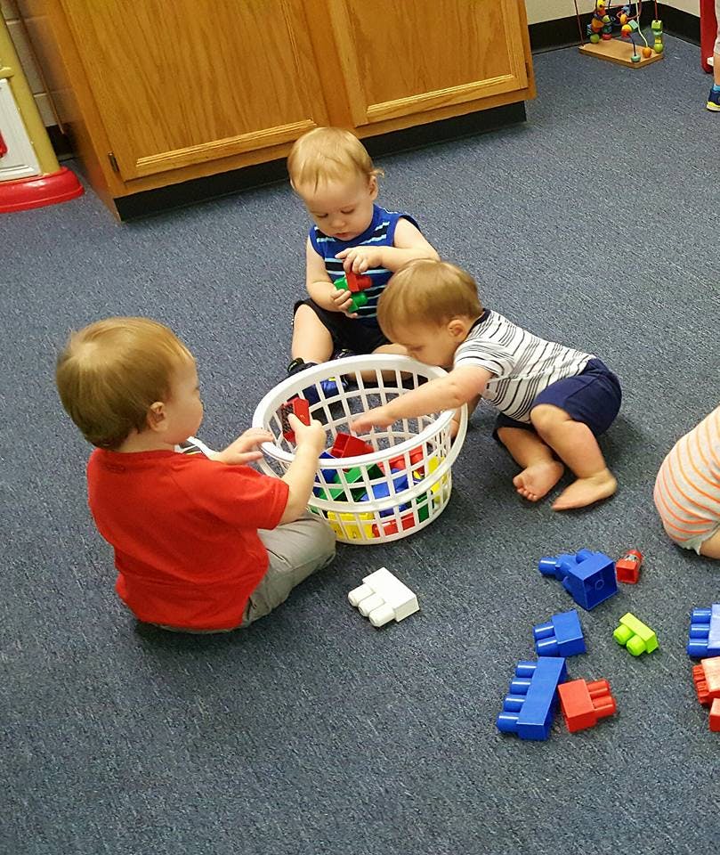 Three children playing with colorful blocks and a basket on the floor