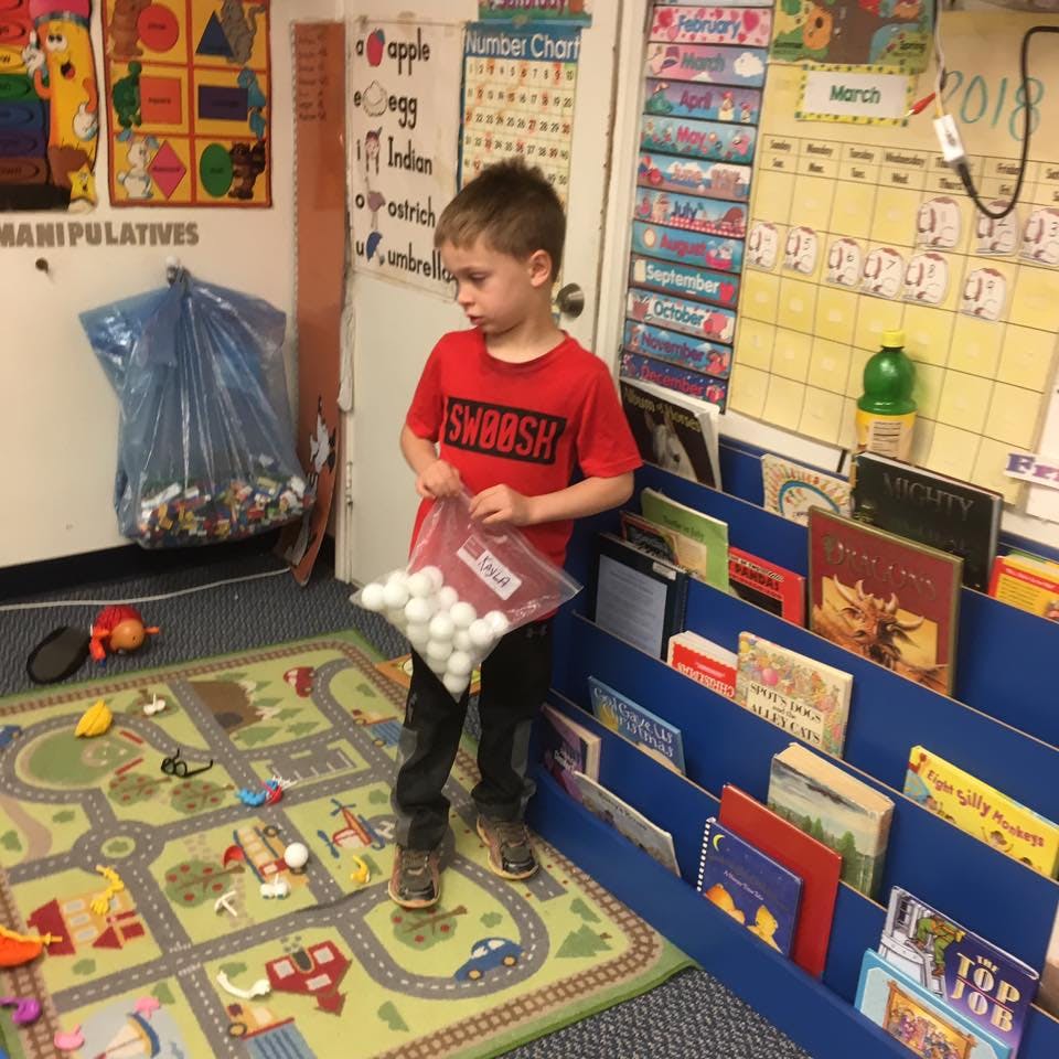Child holding a bag of white pom-poms in a classroom