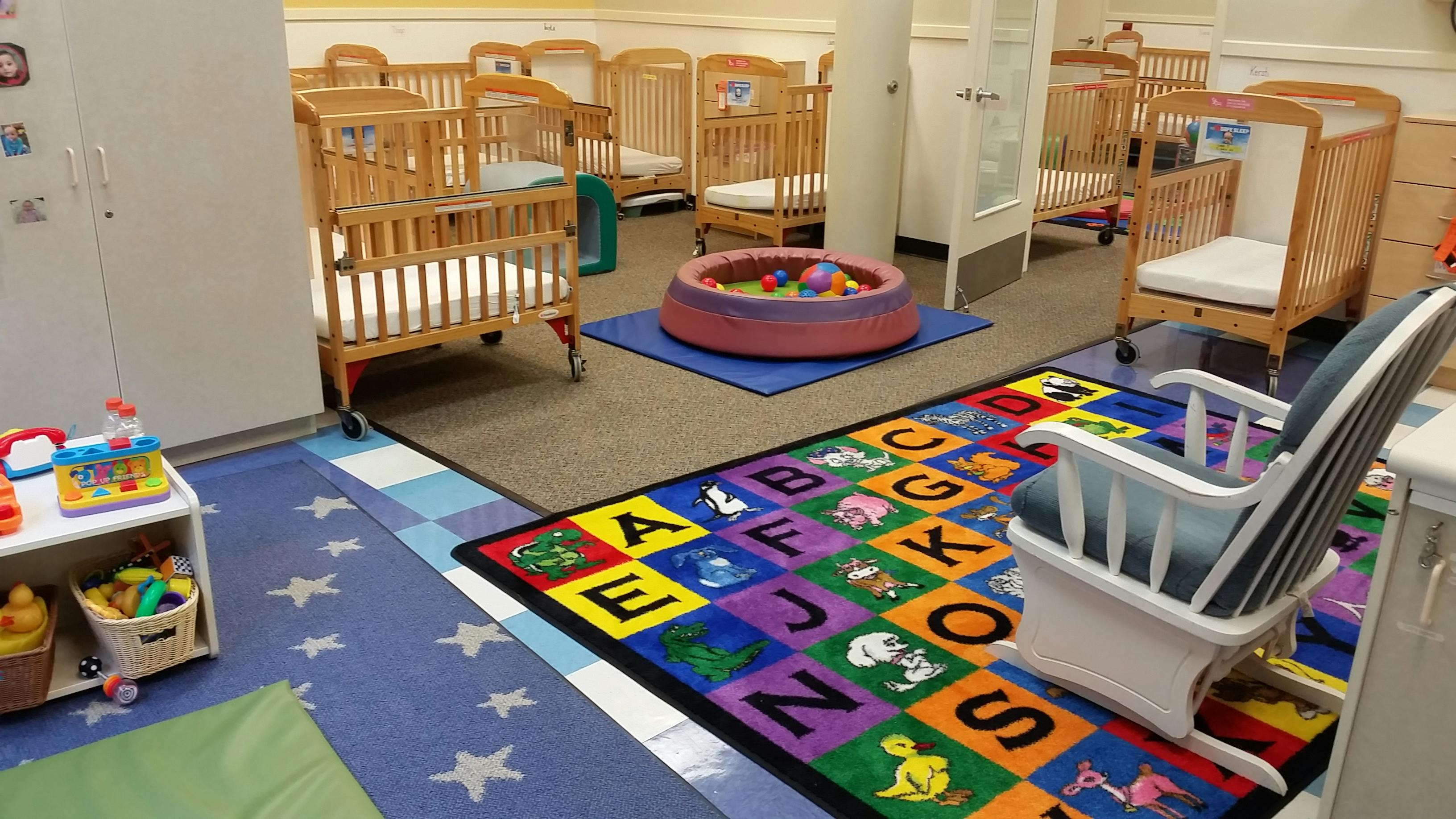 A room with multiple wooden cribs, an alphabet rug, and a ball pit
