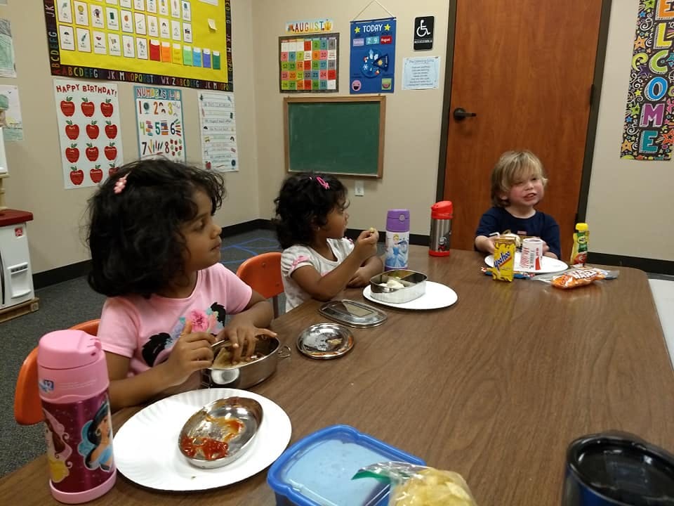 Three children eating at a table in a classroom