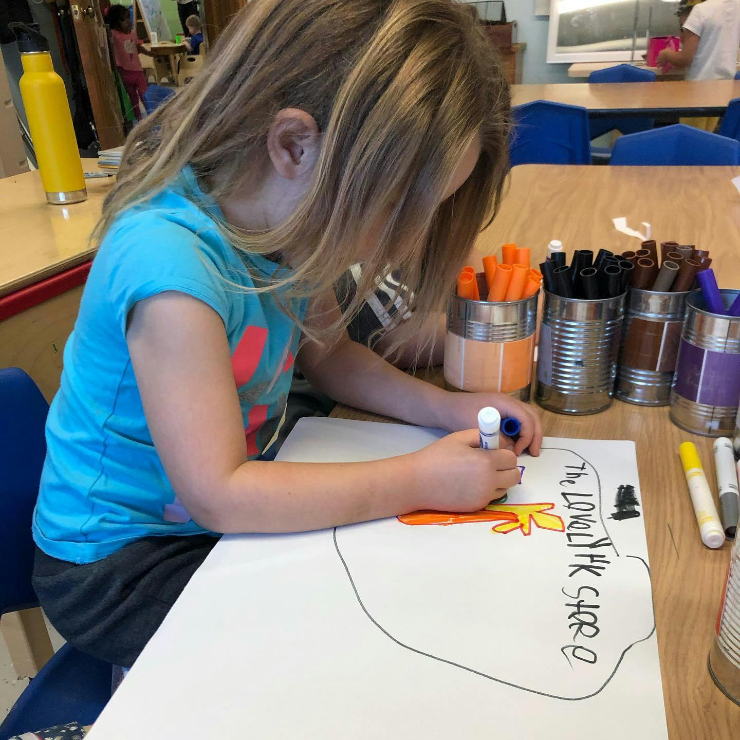 Child drawing on paper with markers at a table