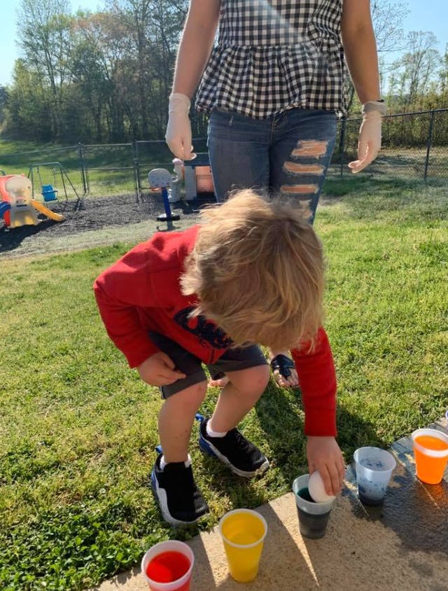 Child dipping an egg into a cup of liquid outdoors