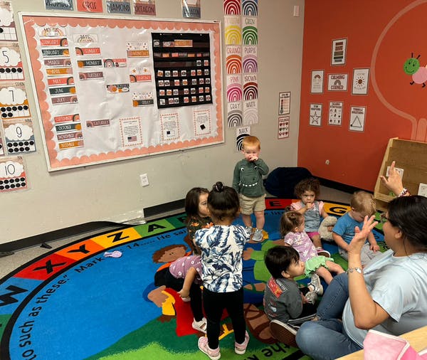 Adult and children sitting on a colorful rug in a classroom