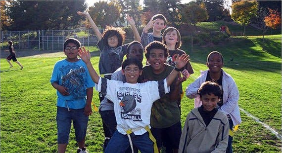 Group of children on a grassy field, some with arms raised