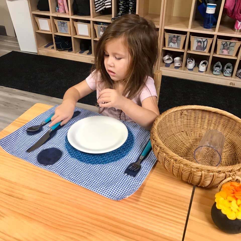 Child setting a table with a plate and utensils