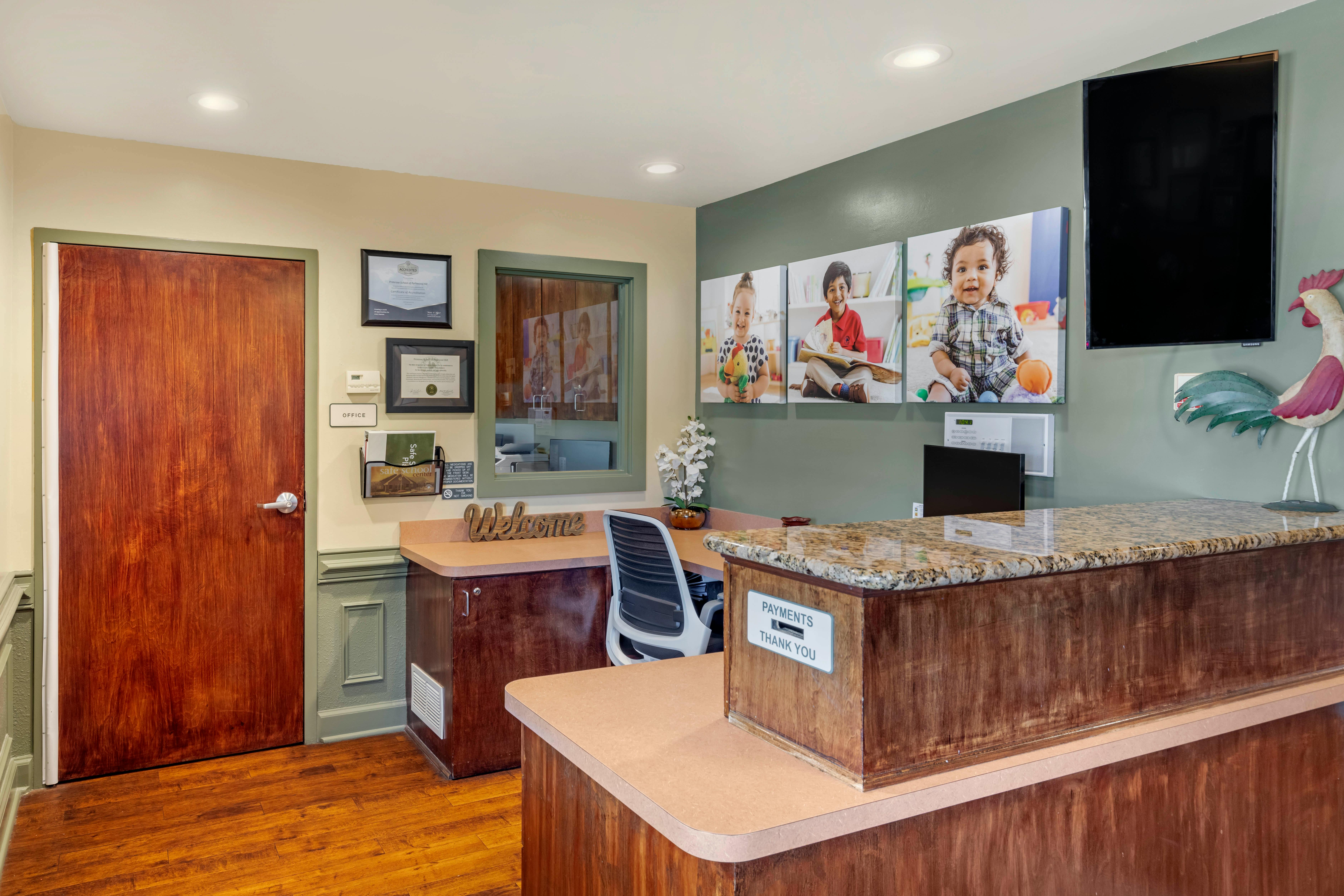 Reception area with a wooden welcome desk, office sign, and children's photos