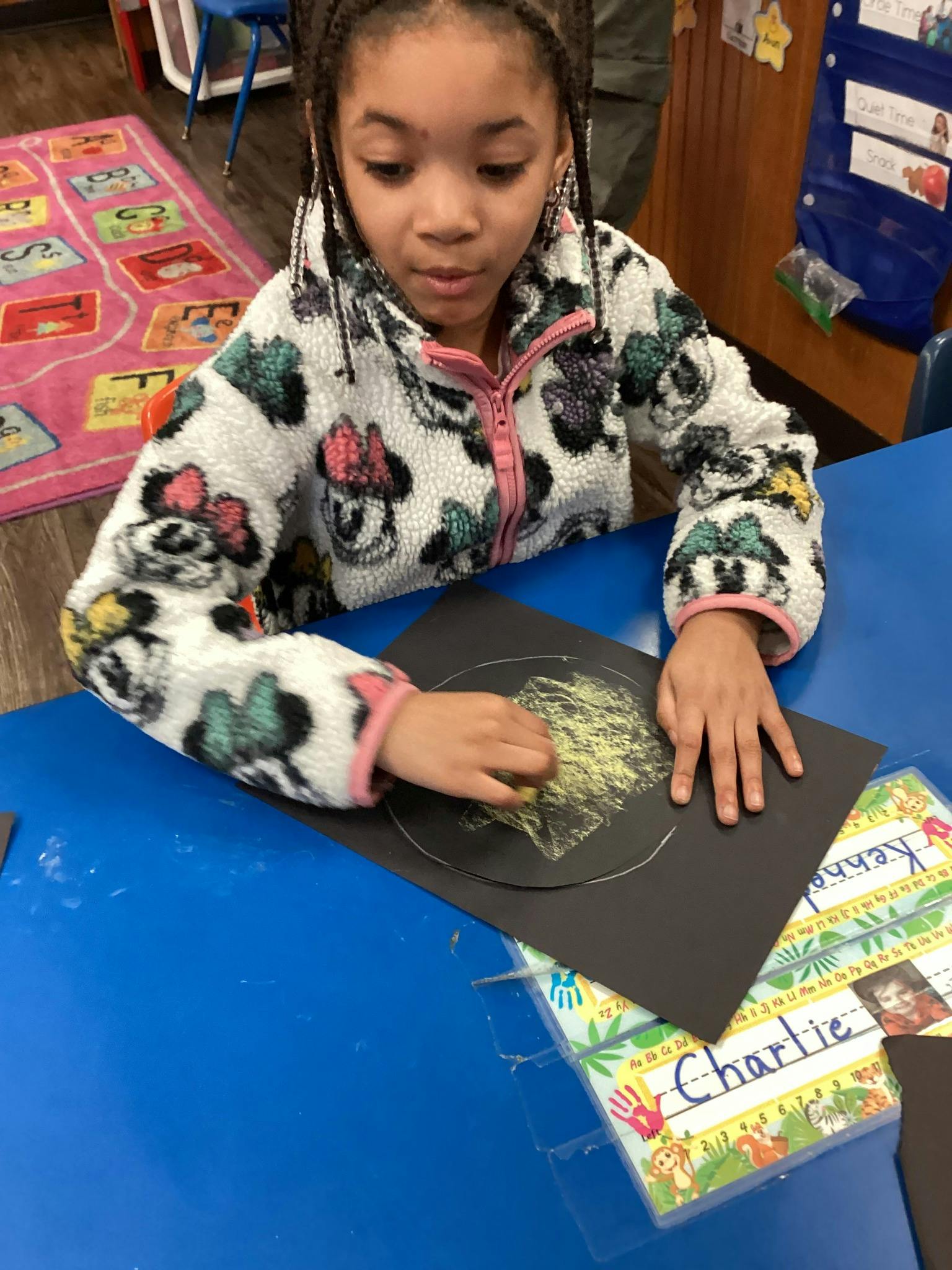Child drawing on black paper at a blue table