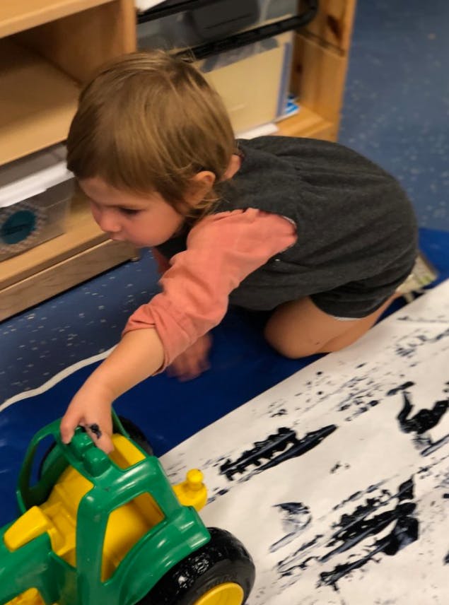 Child kneeling and playing with a toy tractor on paper with paint marks
