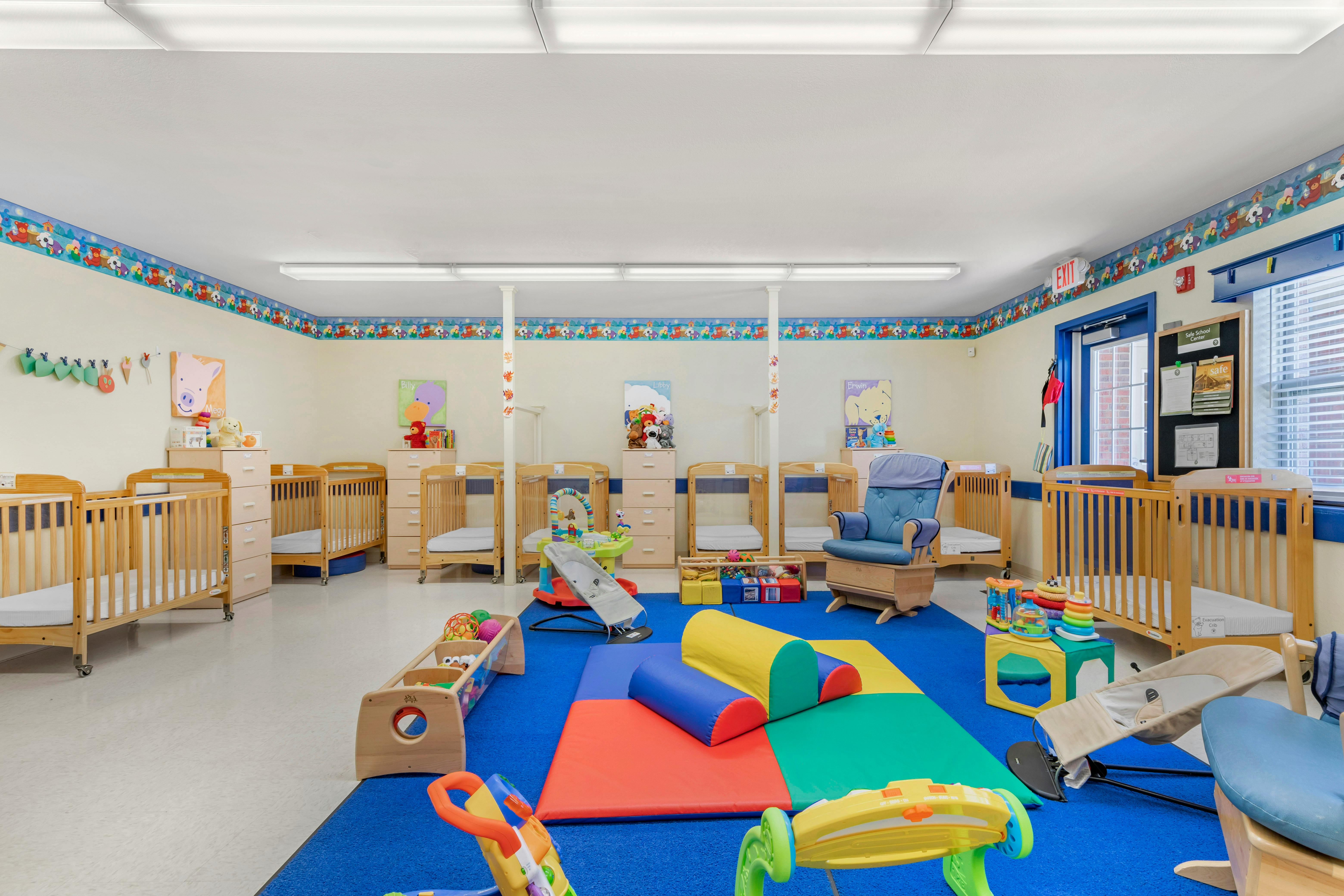 Daycare room with multiple cribs, a blue rug, colorful play mats, and toys