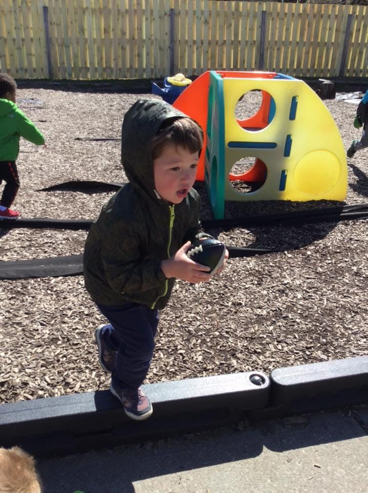 Child in a hooded jacket holding a football on a playground
