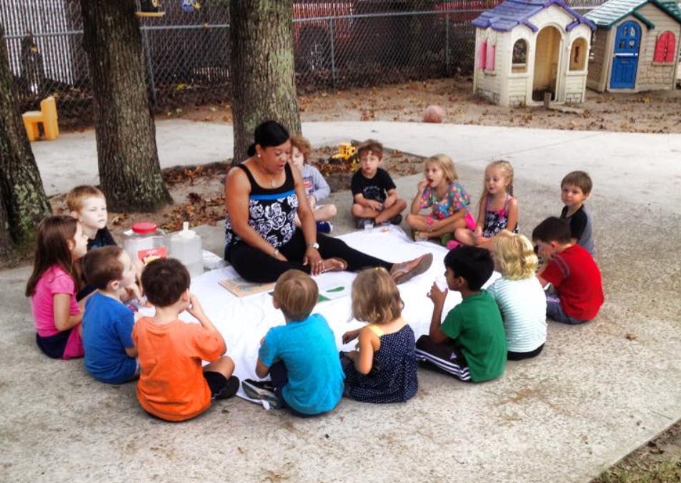 Person sitting on ground with children in a circle around them