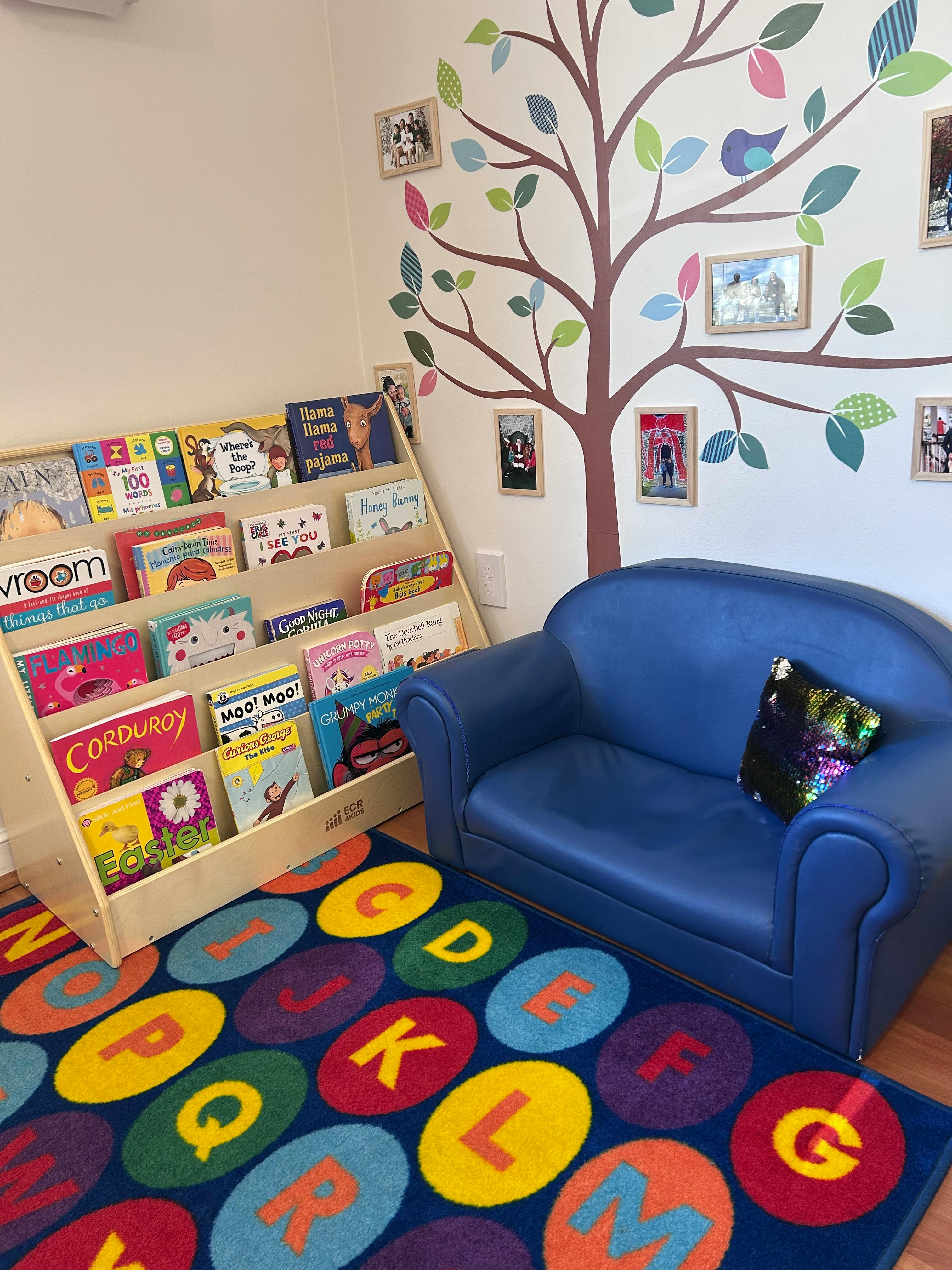 Children's reading nook with a bookshelf, blue couch, and alphabet rug