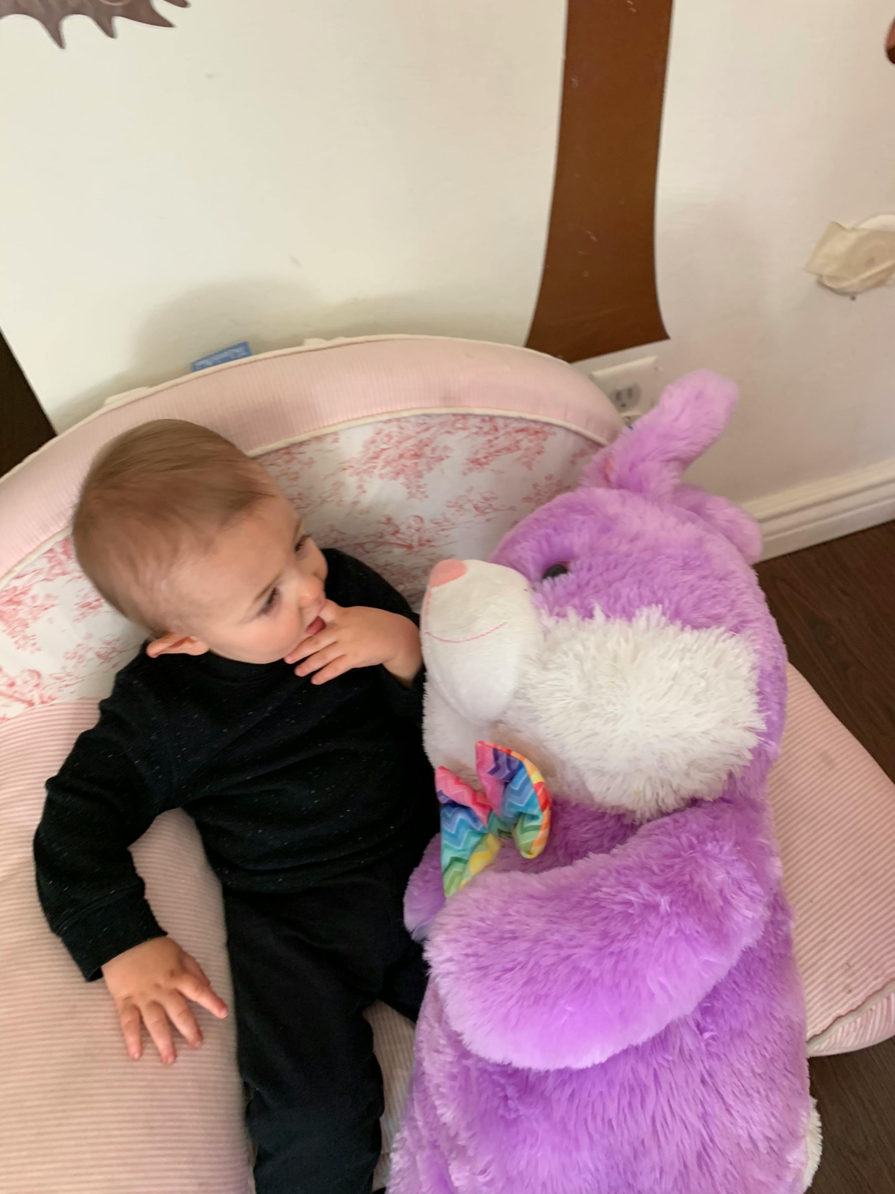 Child lying down next to a large purple stuffed animal