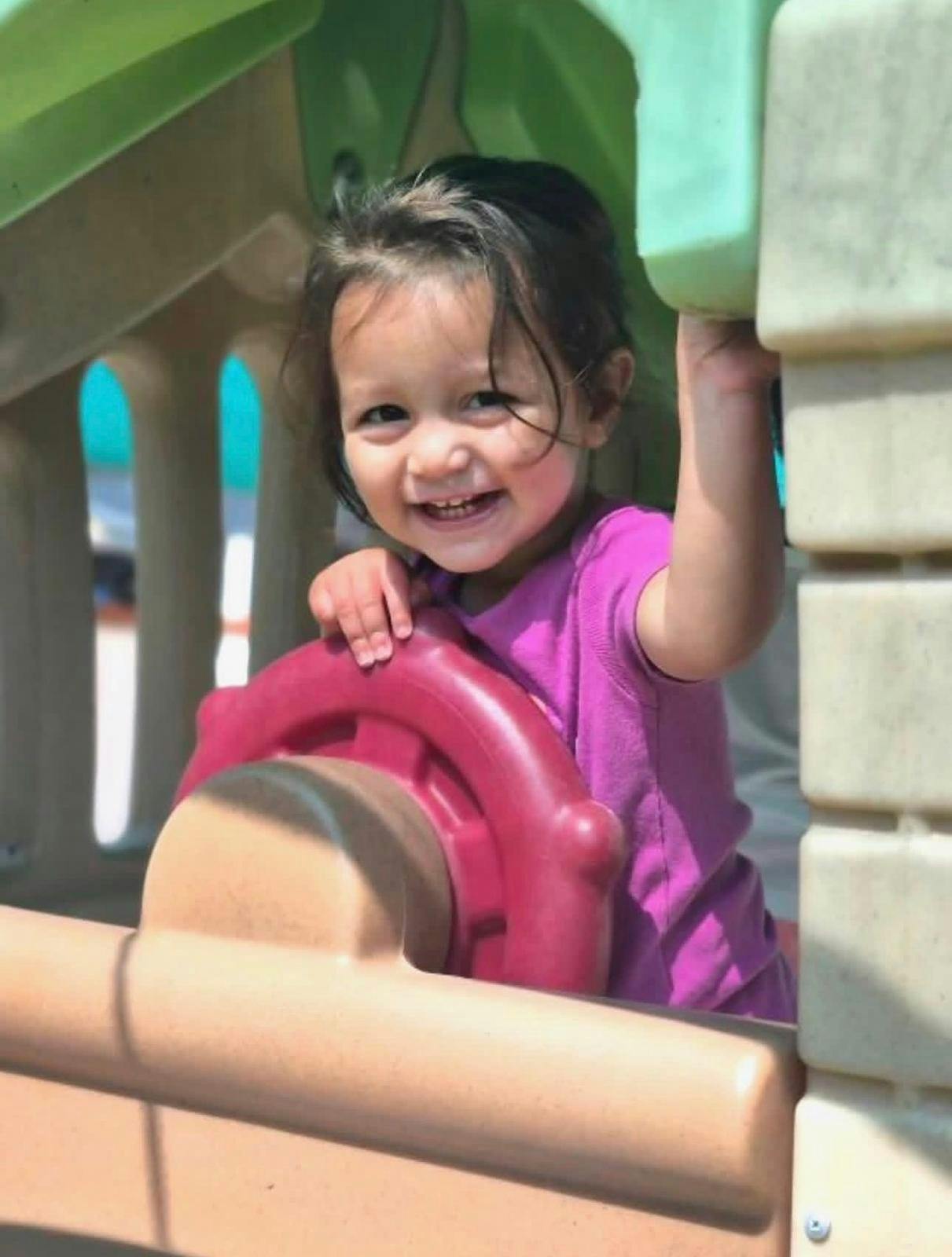 Child standing in a play structure and holding onto a toy steering wheel