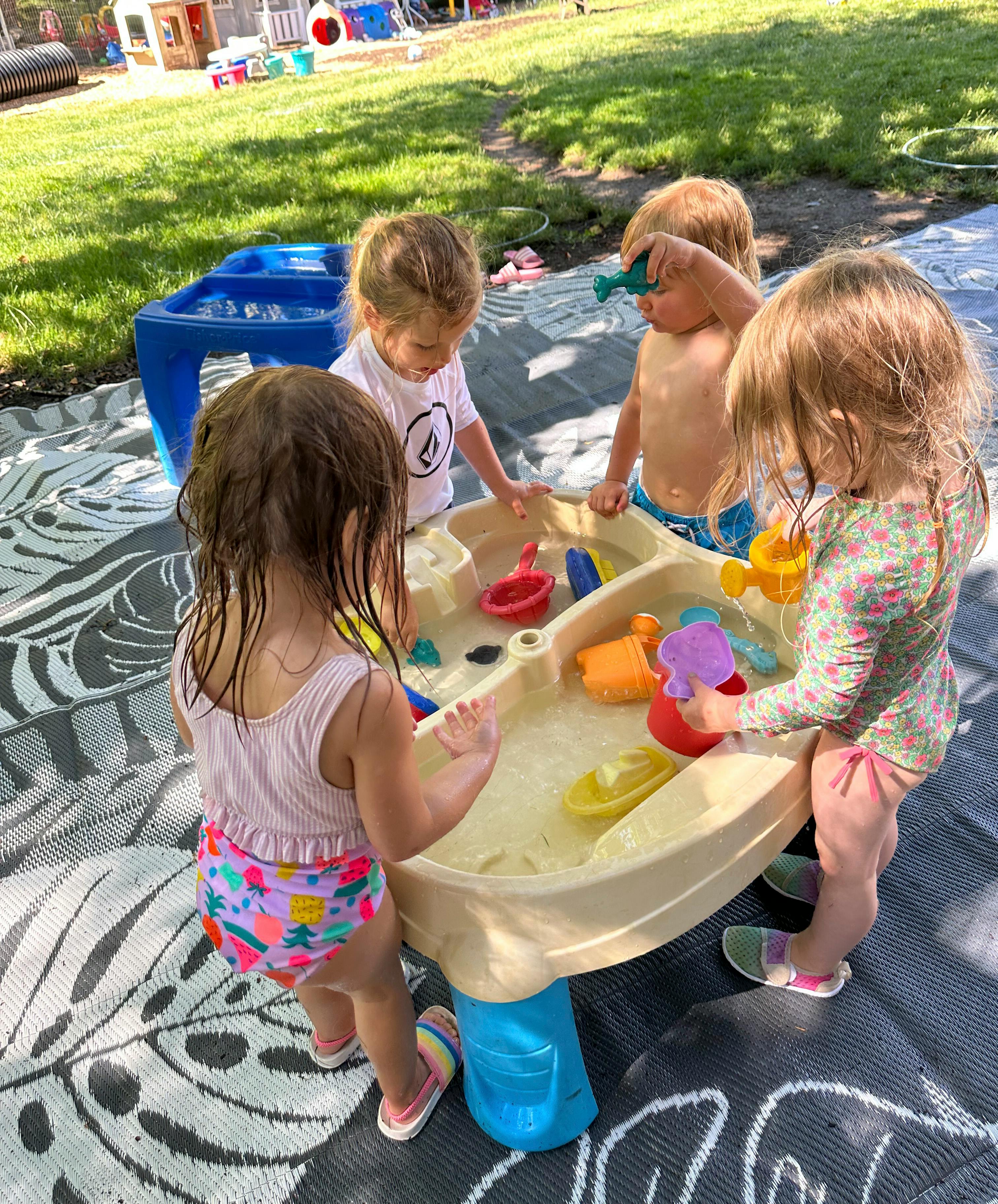 Four children playing with toys in a water table outdoors
