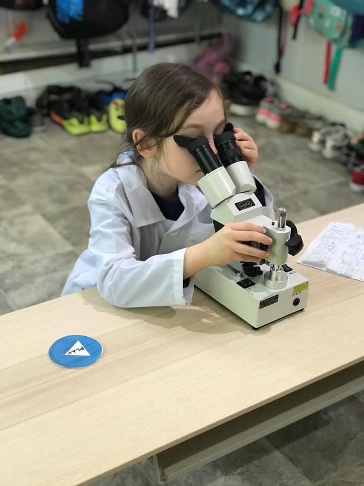 Child in a lab coat looking into a microscope