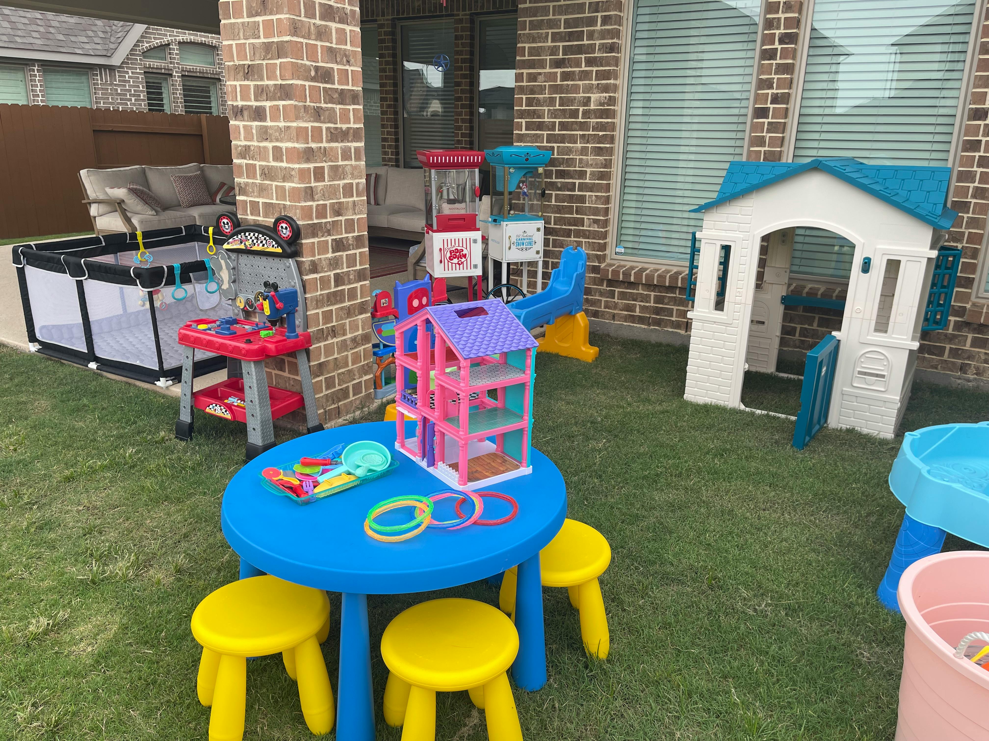 Outdoor play area with a blue table, yellow stools, and various toys
