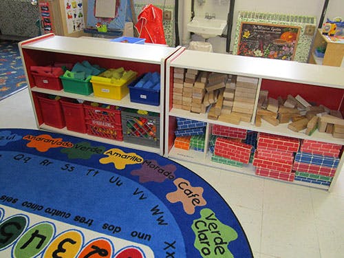 Shelves with colorful bins and wooden blocks next to a blue rug with letters