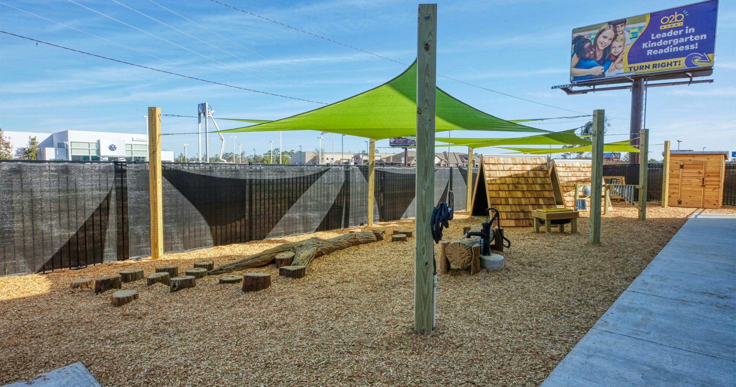 Outdoor play area with wood chips, shade covers, and a small shed