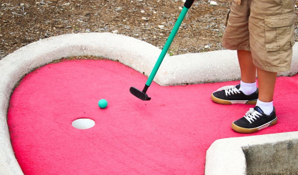 Person playing miniature golf with a green putter and blue ball
