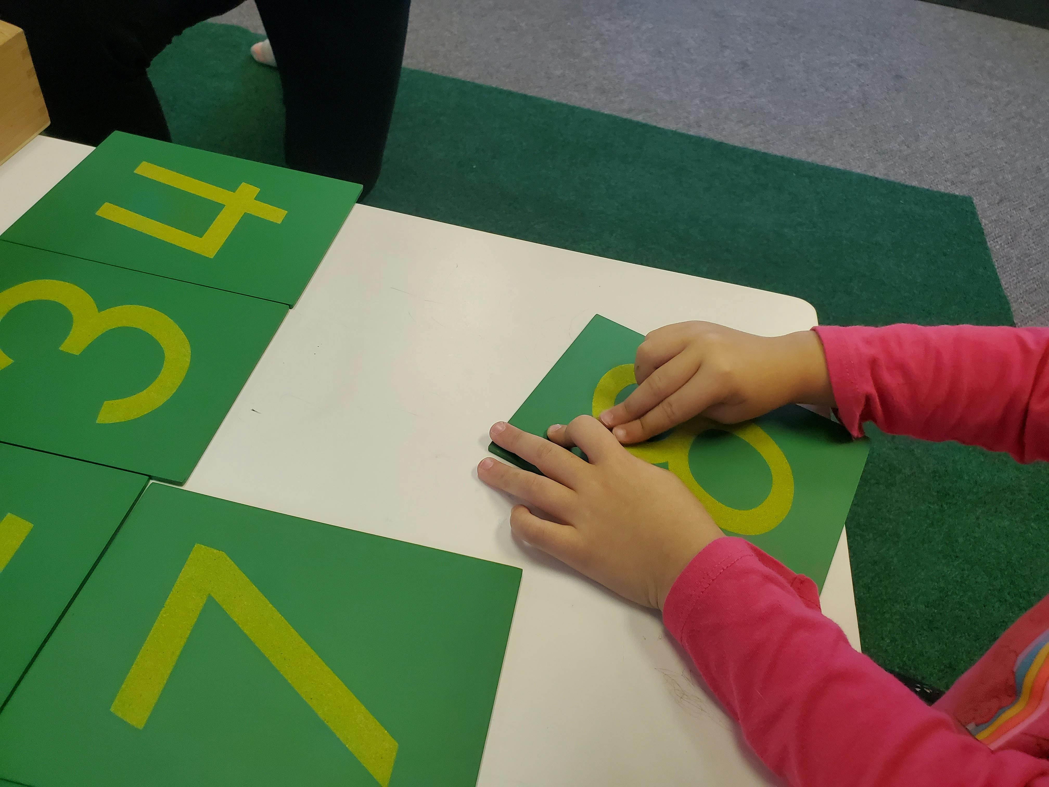 Child's hands touching a green number card with a yellow number