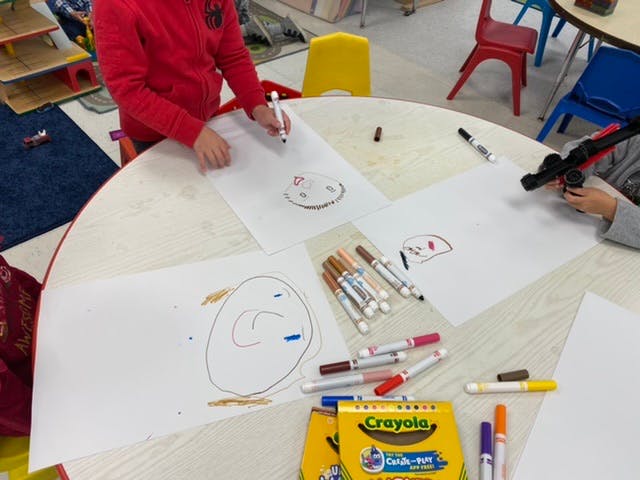Person drawing on paper with markers at a table