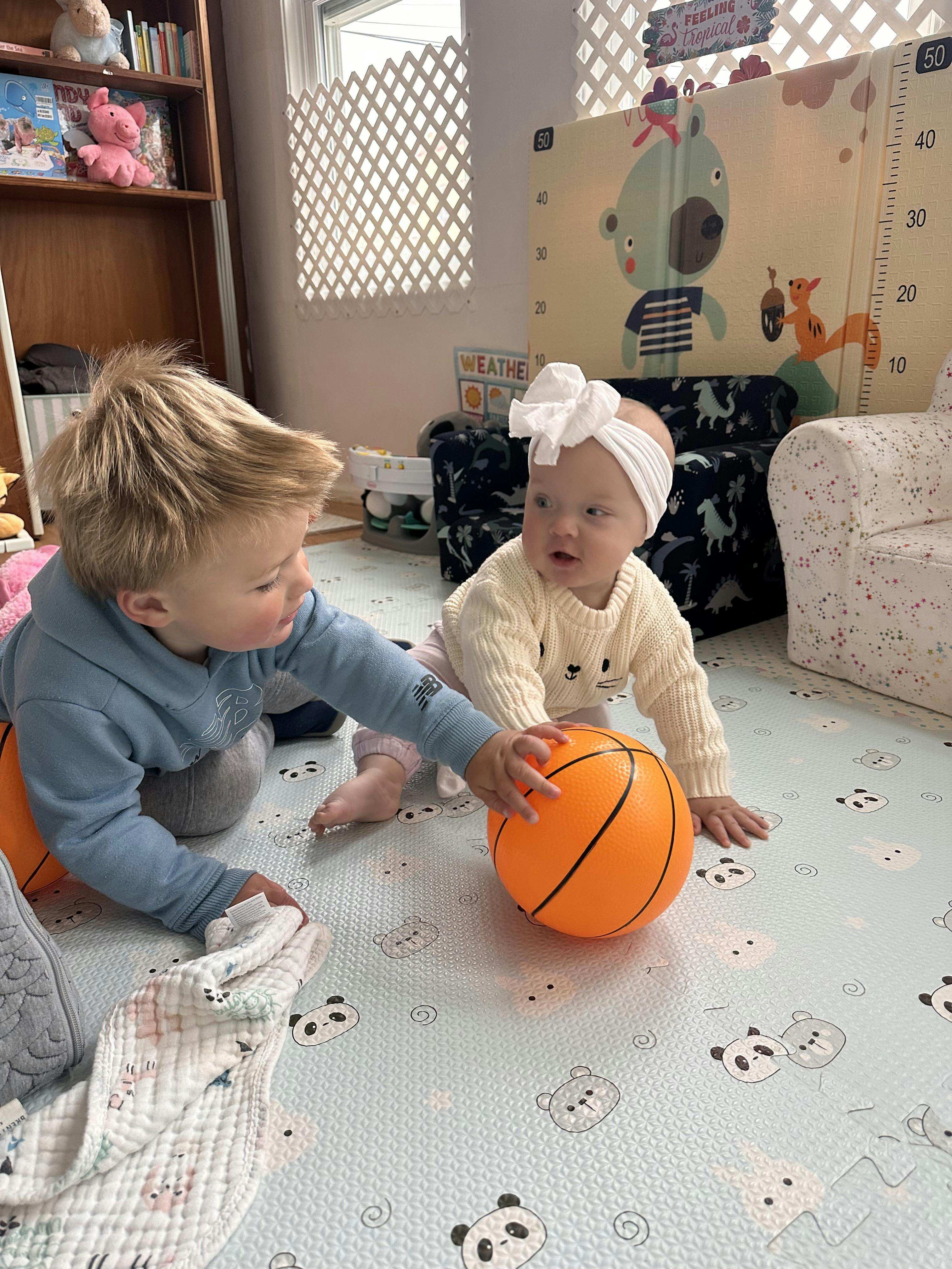 two children on a panda-patterned mat playing with an orange basketball