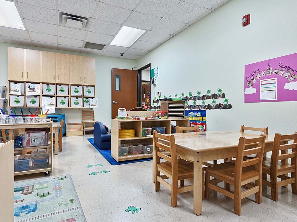 Classroom with small wooden tables and chairs, storage cabinets, and wall decorations