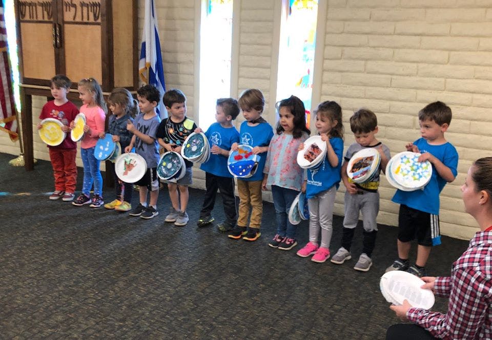 Children standing in a line holding paper plates with designs