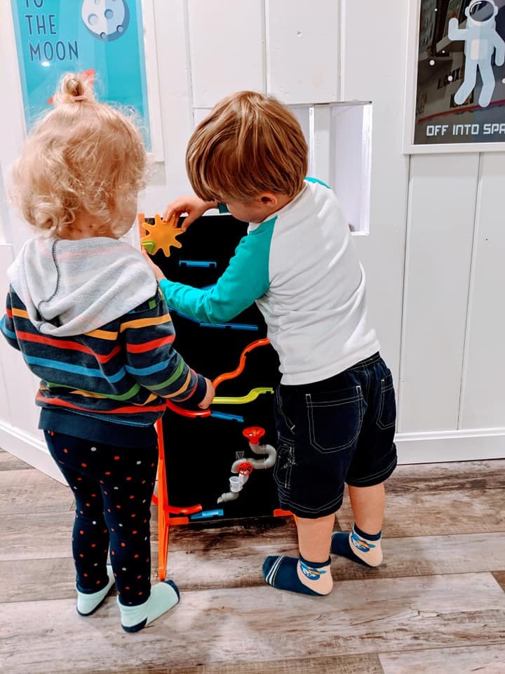 Two children playing with a wall-mounted activity board
