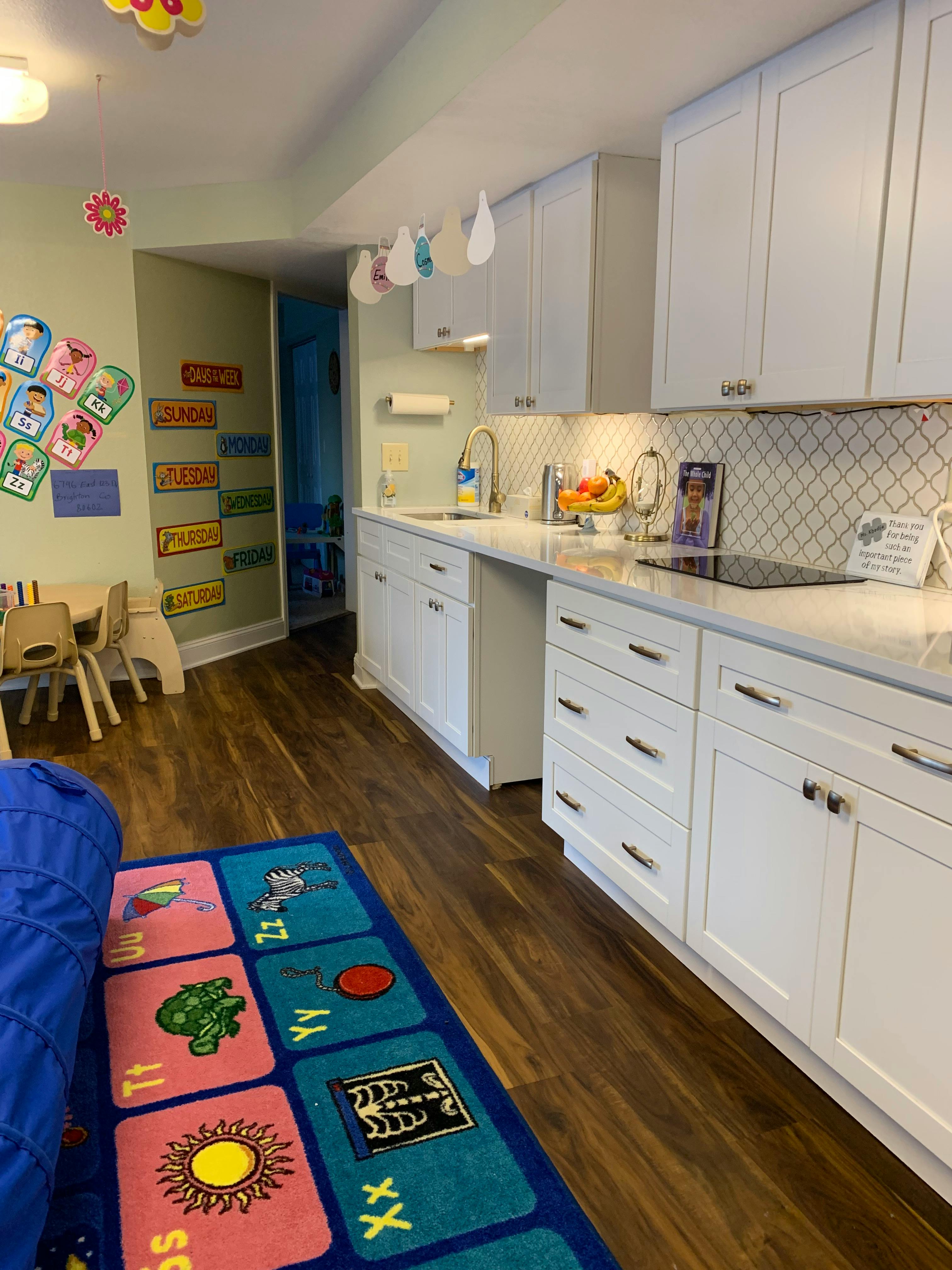 Kitchen area with white cabinets and a children's play area with a colorful rug