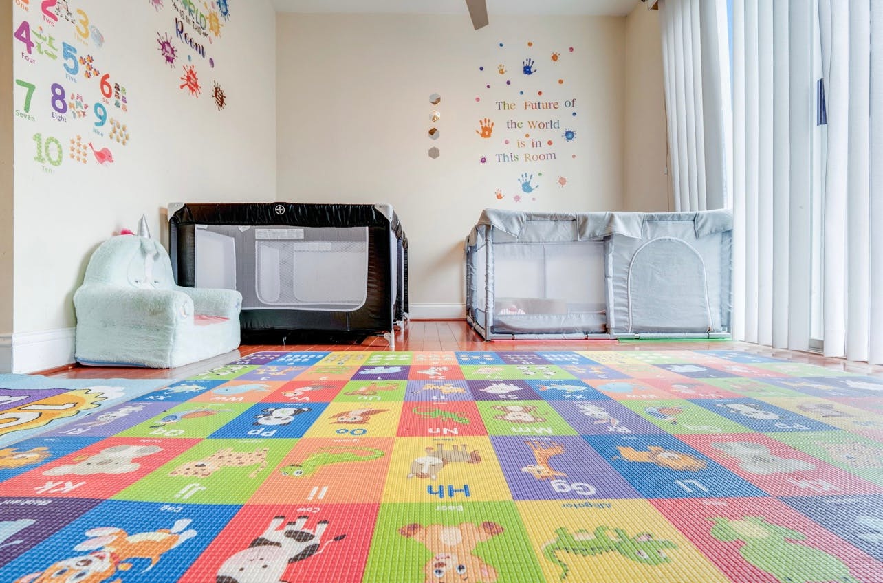 Two playpens in a room with a colorful alphabet and number mat